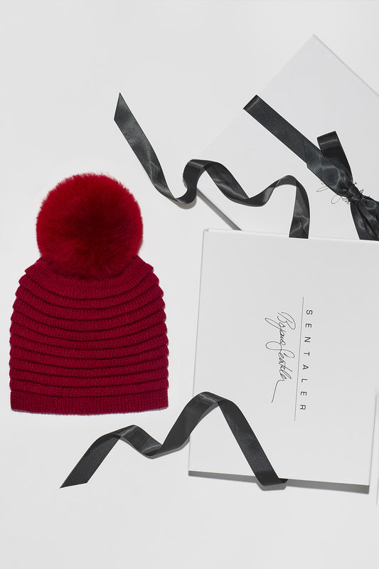 Sentaler Adult Ribbed Hat With Oversized Fur Pompon featured in Baby Alpaca and available in Garnet Red. Seen as Holiday Flat Lay.