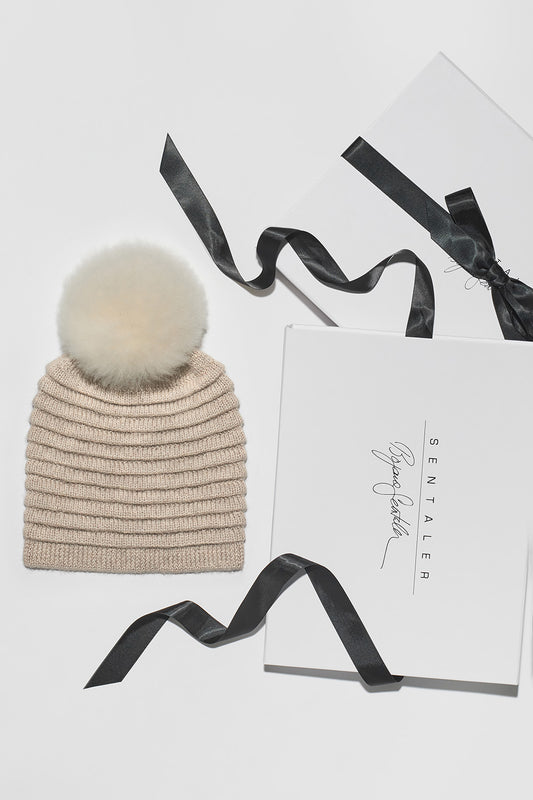 Sentaler Adult Ribbed Hat With Oversized Fur Pompon featured in Baby Alpaca and available in Light Taupe. Seen as Holiday Flat Lay.