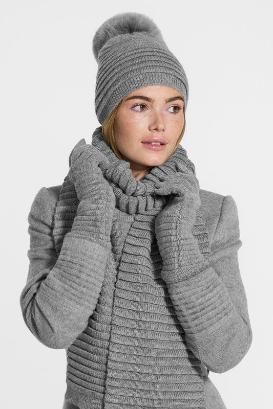 Sentaler Adult Ribbed Hat With Oversized Fur Pompon, Ribbed Scarf and Ribbed Gloves featured in Baby Alpaca and available in Grey. Seen from side above the waist on model.