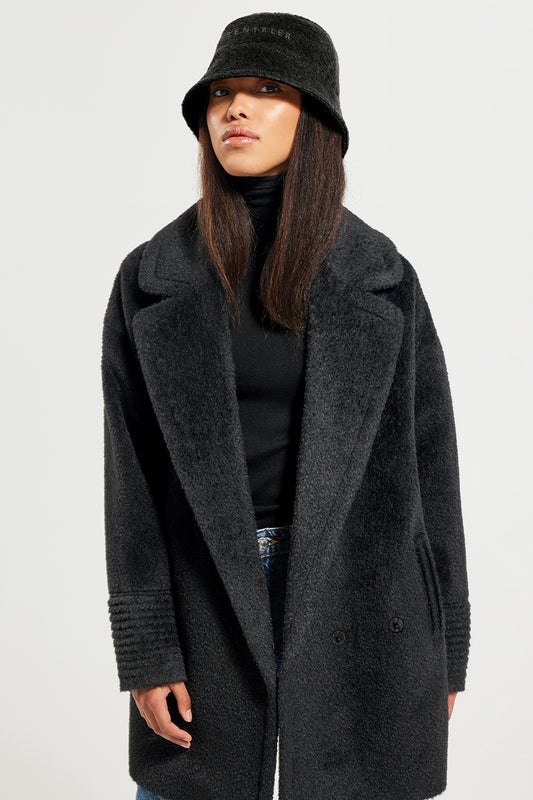 Sentaler Bouclé Alpaca Bucket Hat and Bouclé Alpaca Mid Length Oversized Notched Collar Coat featured in Bouclé Alpaca and available in Black. Seen from front above the knees on model.