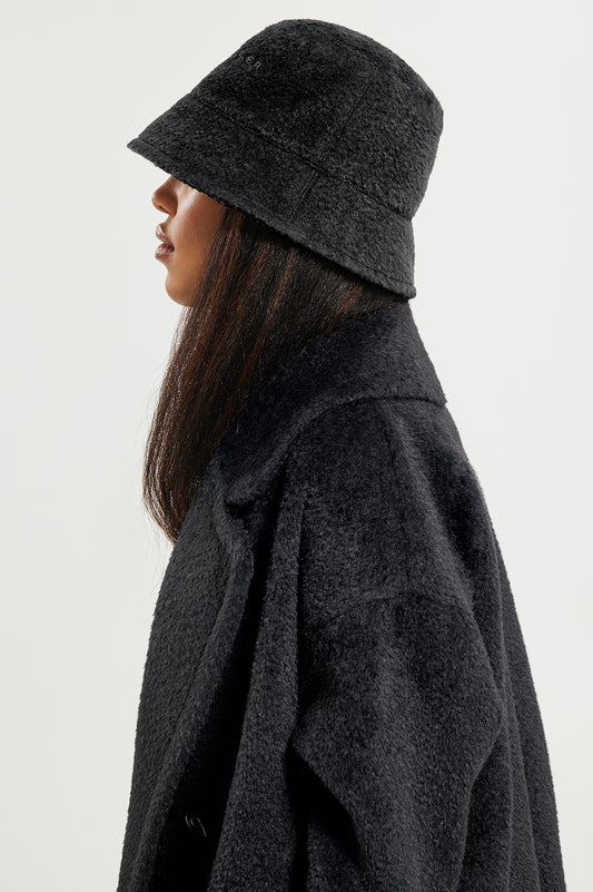 Sentaler Bouclé Alpaca Bucket Hat and Bouclé Alpaca Mid Length Oversized Notched Collar Coat featured in Bouclé Alpaca and available in Black. Seen from side close up on model.